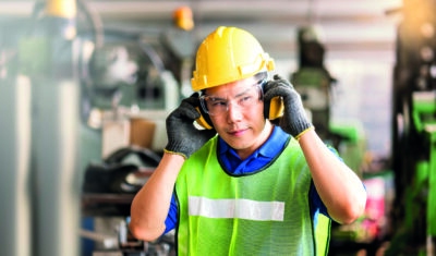 Arbeitnehmer mit Schutzhelm, Schutzbrille, Ohrenschützern und Warnweste.