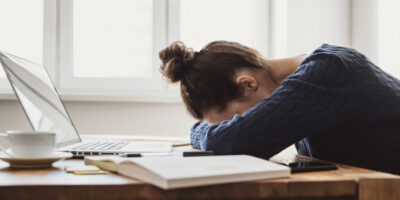 Frau liegt übermüdet mit ihrem Kopf auf dem Schreibtisch.